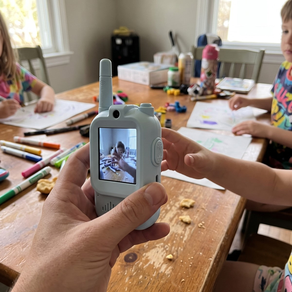 Adult handing a blue Playpal device to a child at a home play table